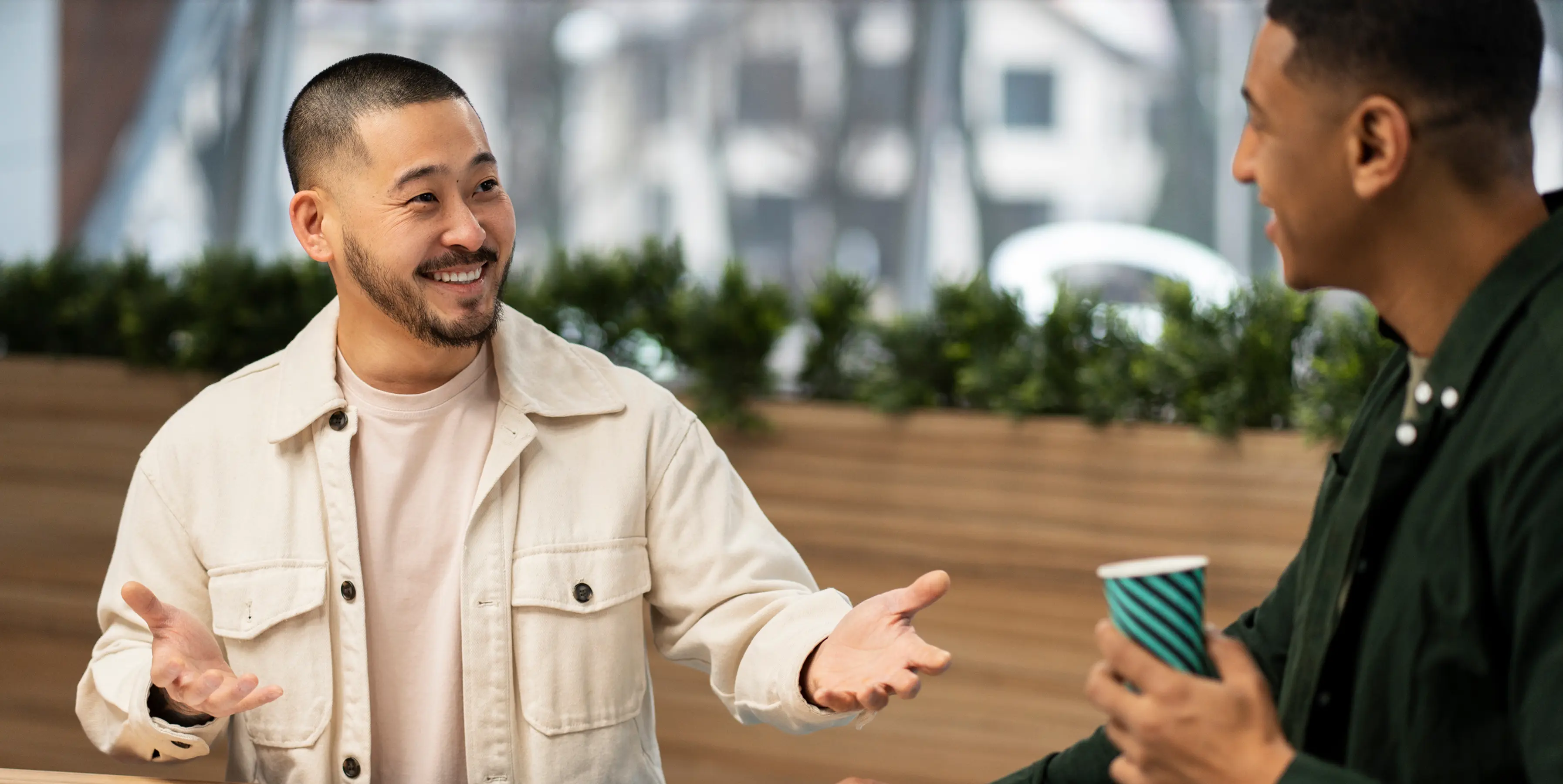 Two men in casual clothes having a friendly conversation, one holding a striped cup.