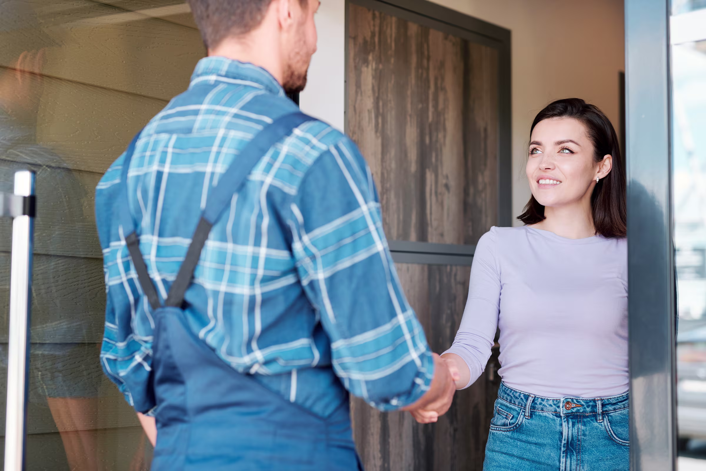 Woman opens door and shakes hands with a man in overalls outside her home.