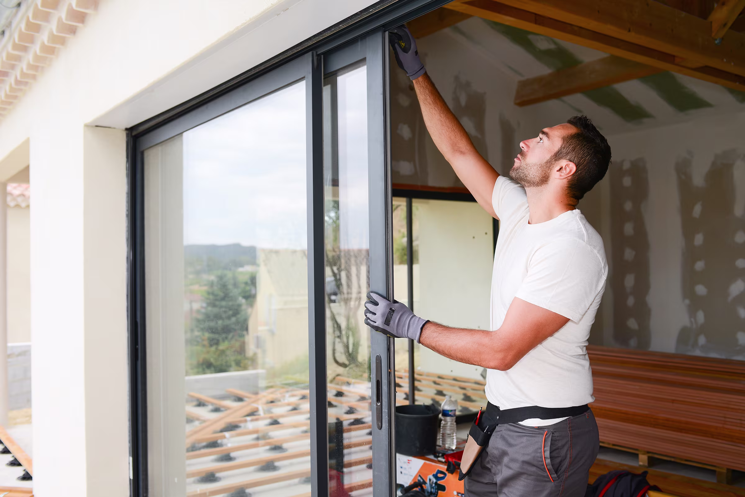 Man in gloves installing a sliding glass door in a house under construction.
