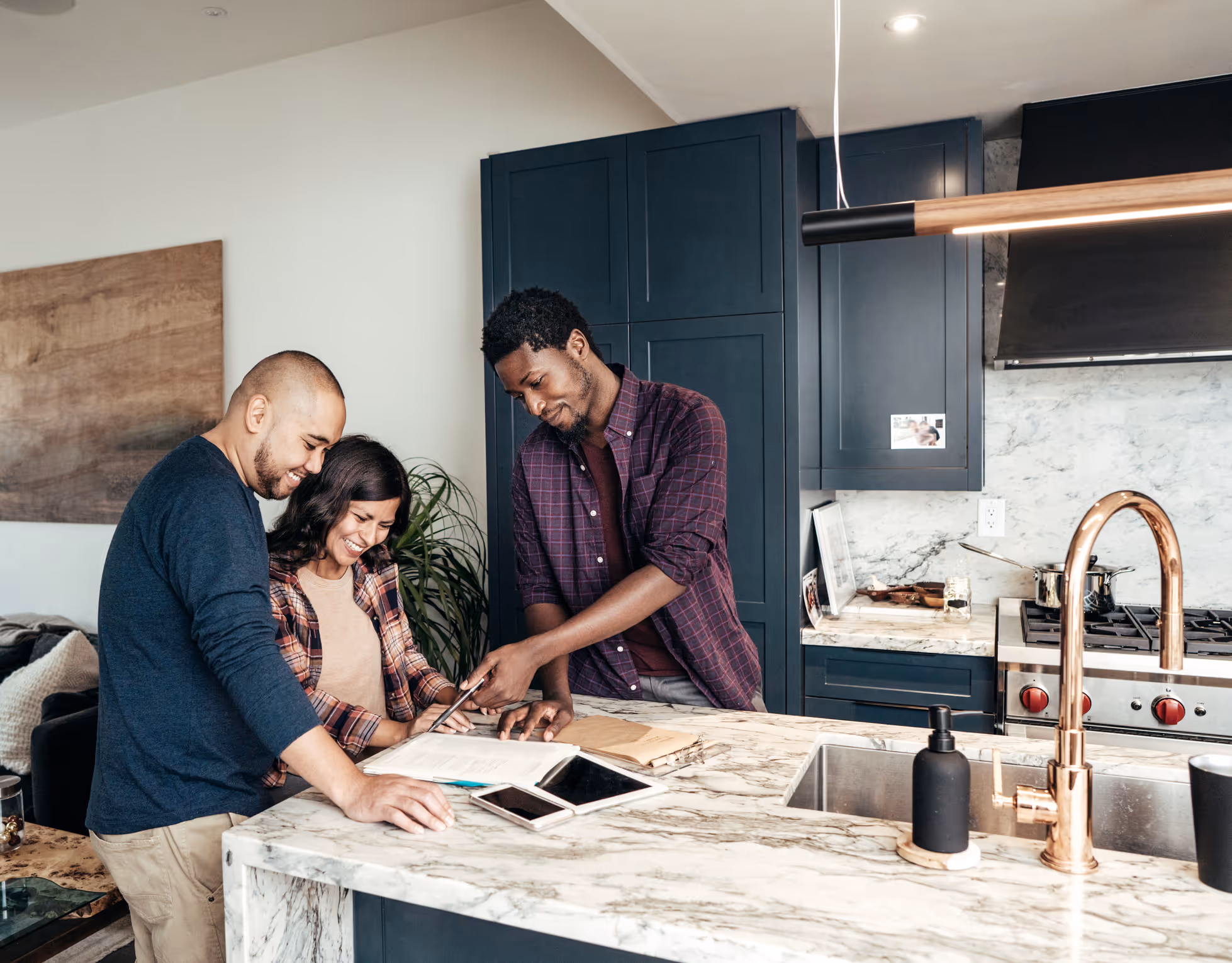 Three people smiling and reviewing papers together at a kitchen island with a marble countertop.