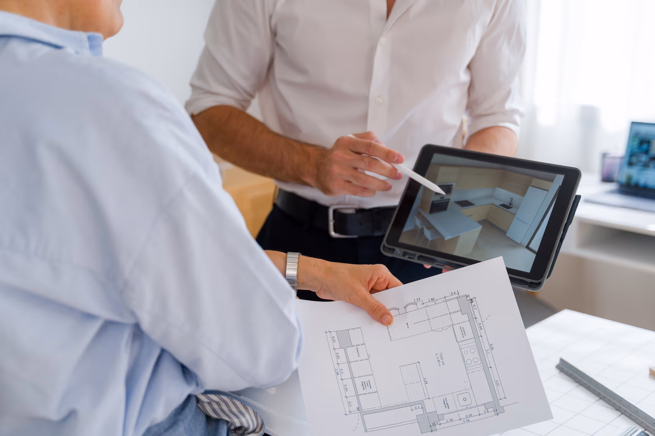 Two people reviewing a kitchen floor plan on paper and a 3D kitchen design on a tablet.