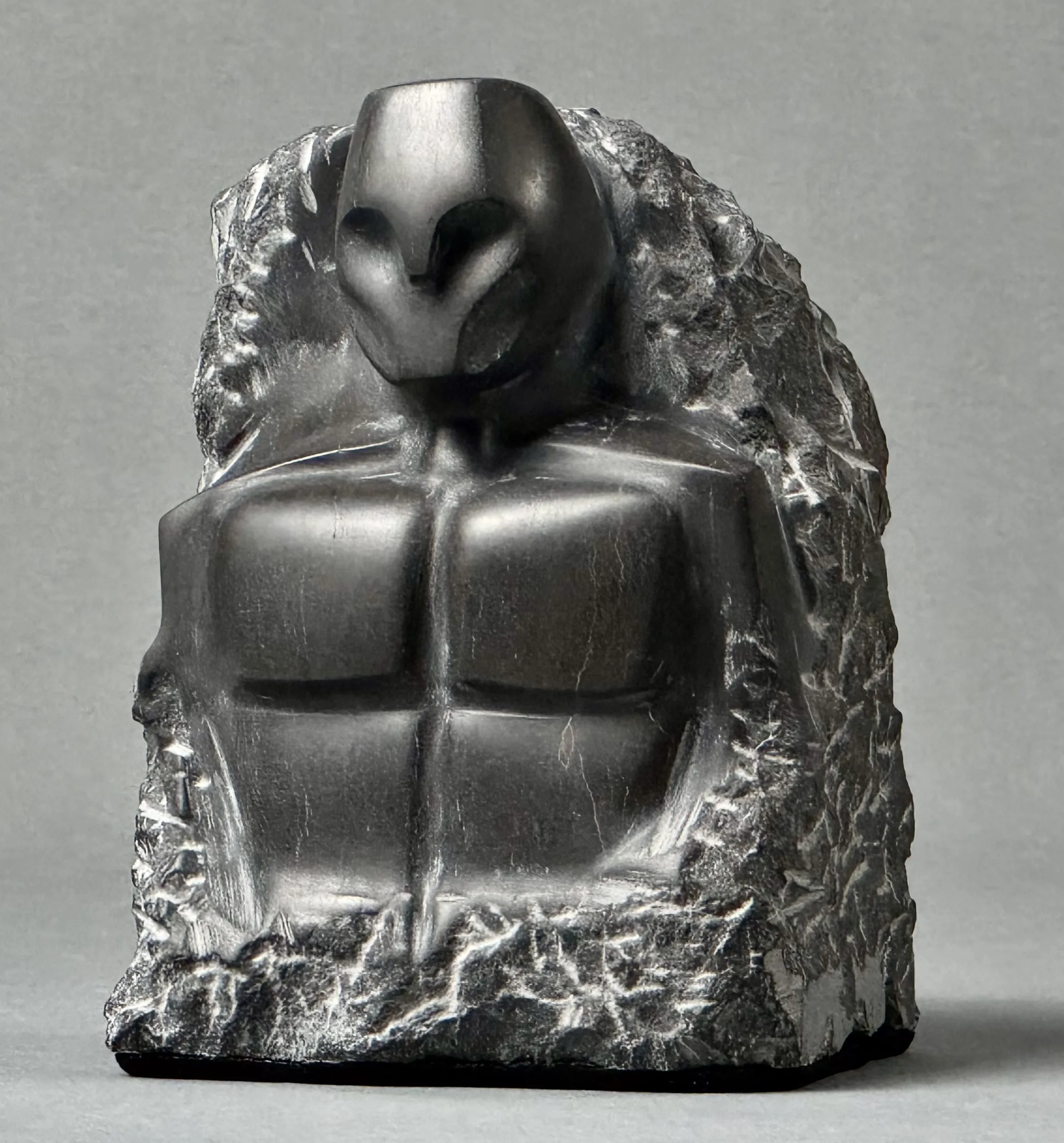 Black stone sculpture of a stylized humanoid torso with a smooth abstract face and rough textured edges.