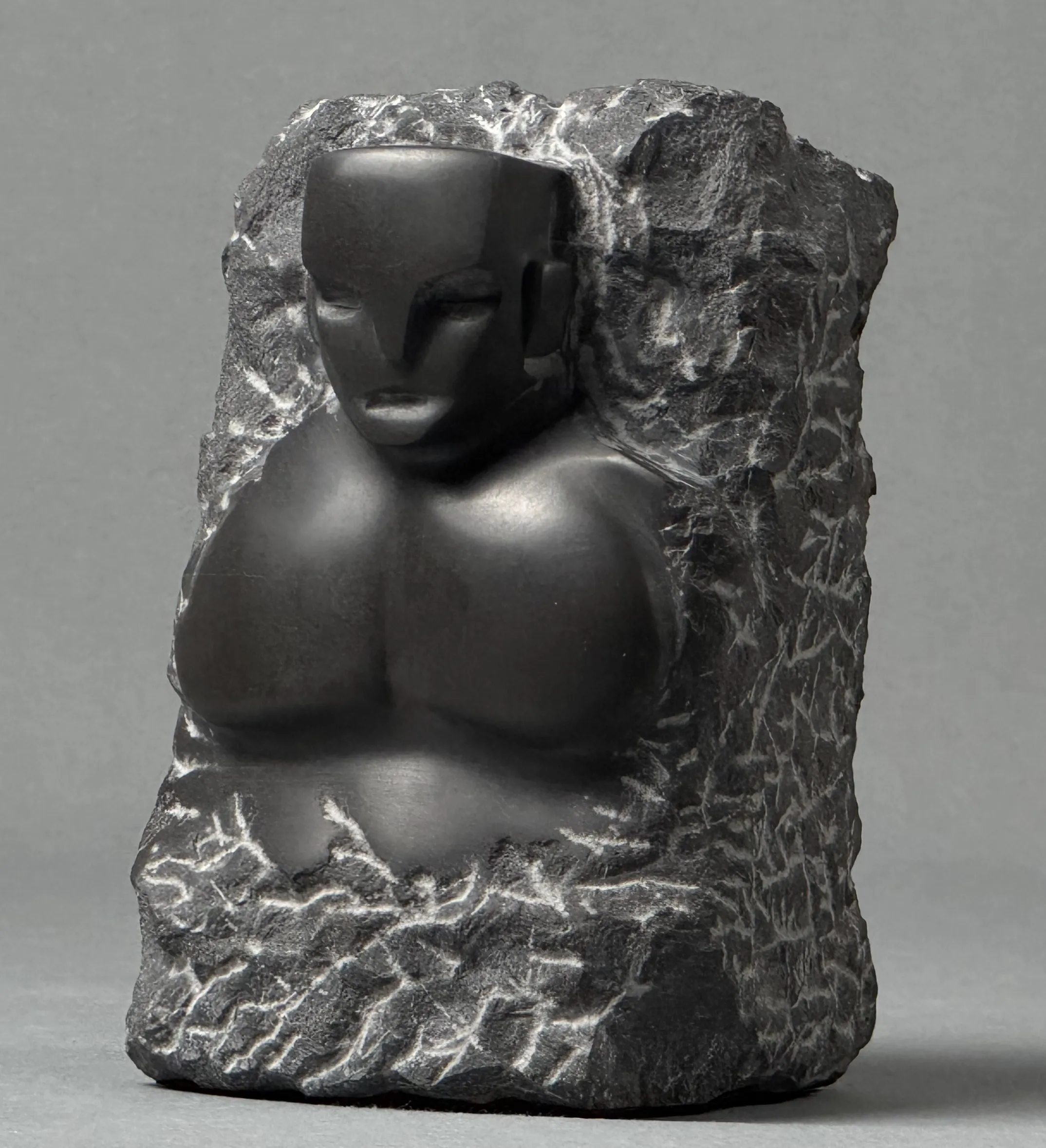 Black stone sculpture of a stylized human torso and head emerging from rough stone.