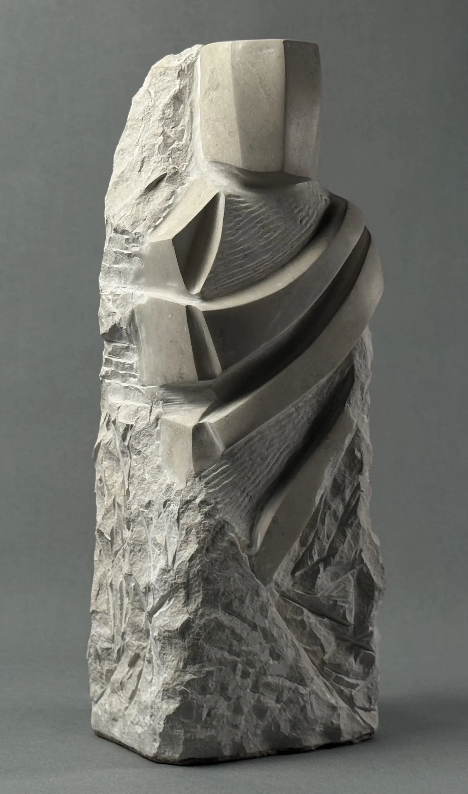 Abstract stone sculpture with geometric shapes and smooth carved surfaces on rough stone block.