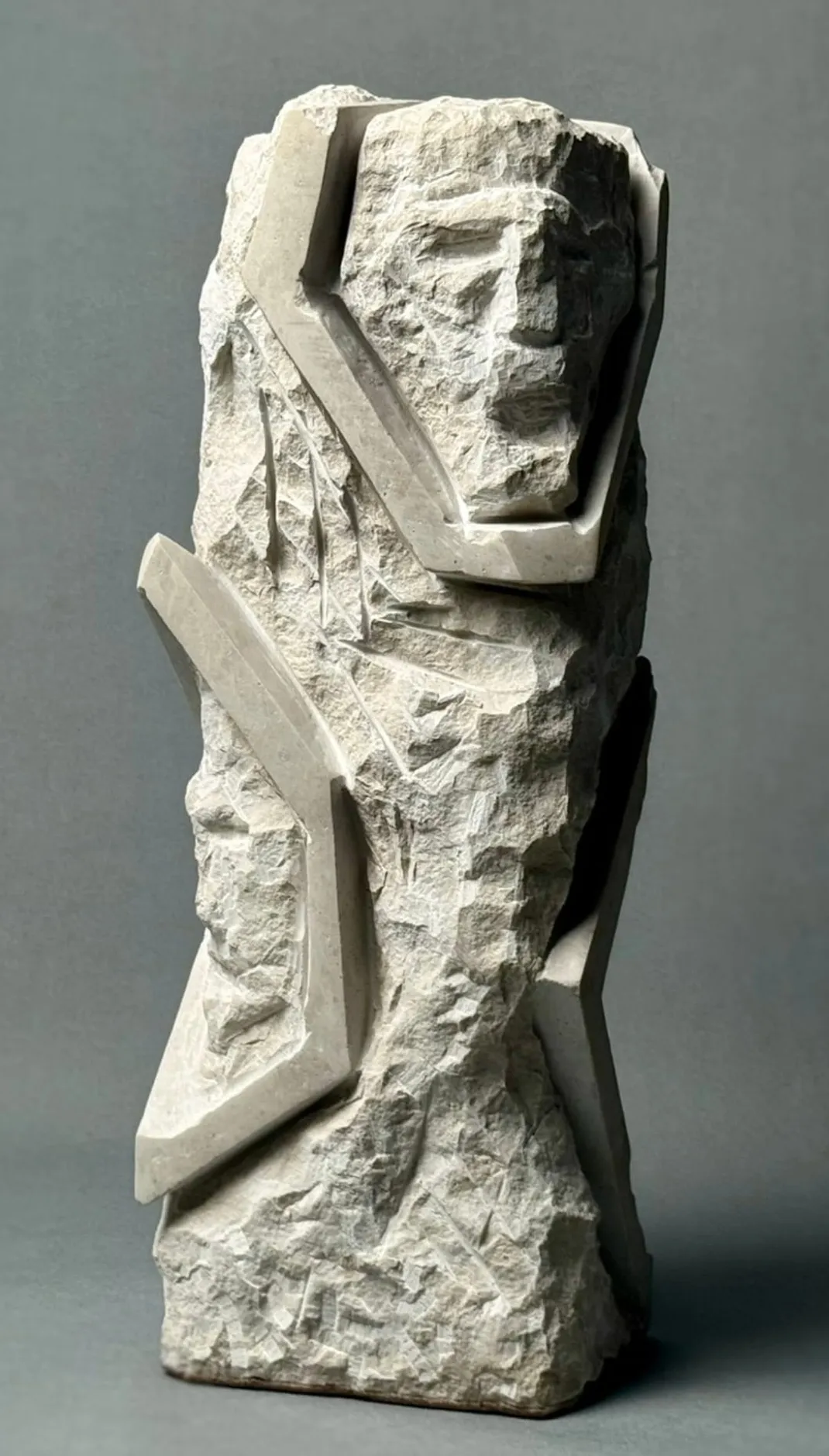 Rough stone sculpture of a human face and abstract geometric shapes in relief.