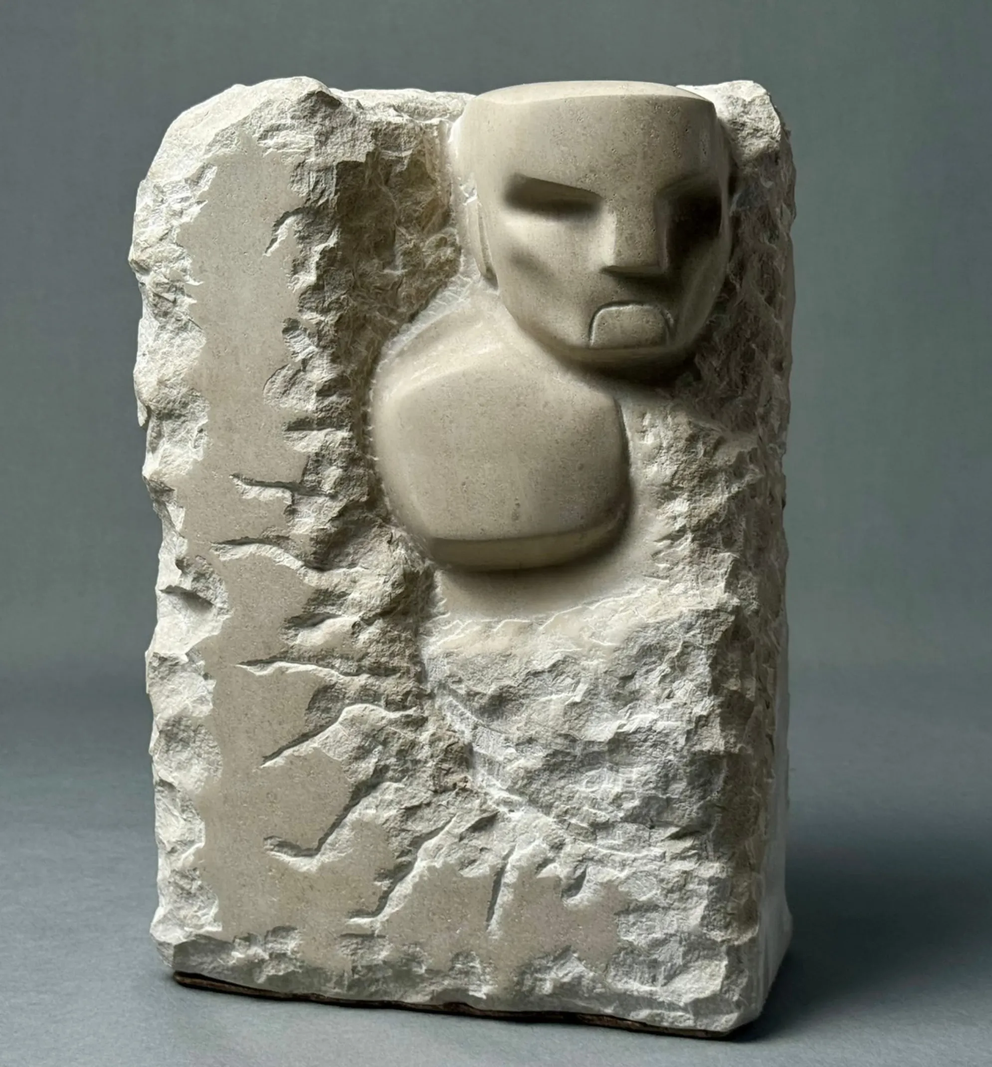 Stone sculpture of a stylized humanoid face and upper torso carved from rough rectangular block.
