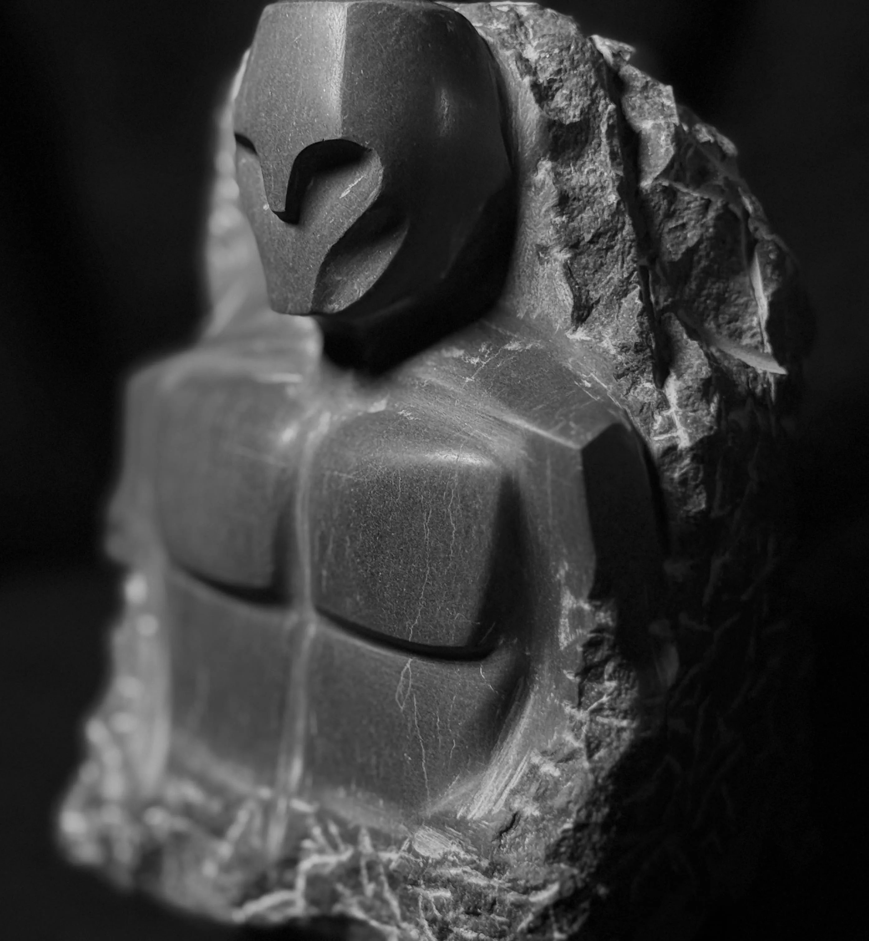 Black stone sculpture of a stylized torso and head with geometric features and rough rock edges.