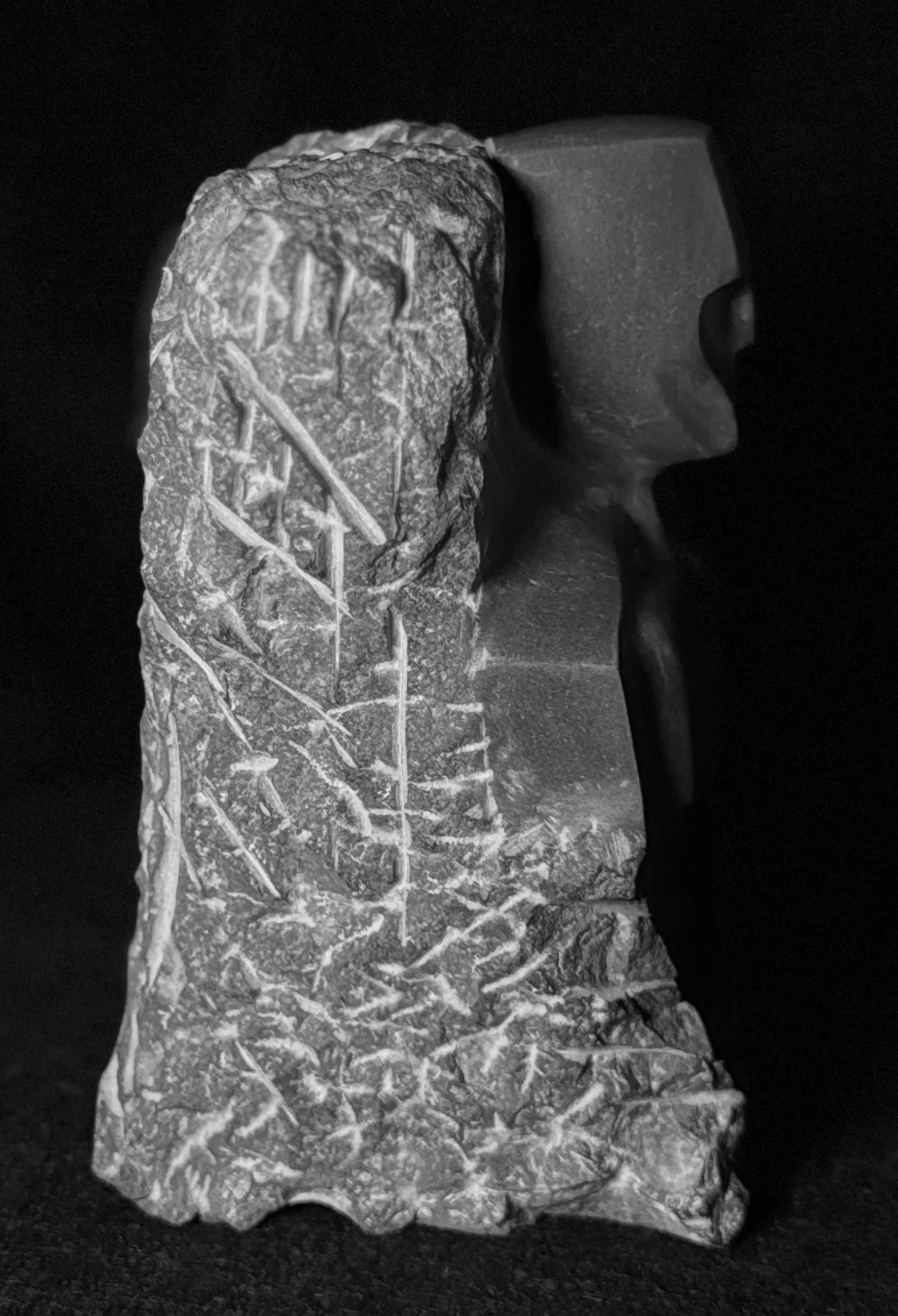 Stone sculpture with rough textured carvings on the left and a smooth abstract figure on the right.