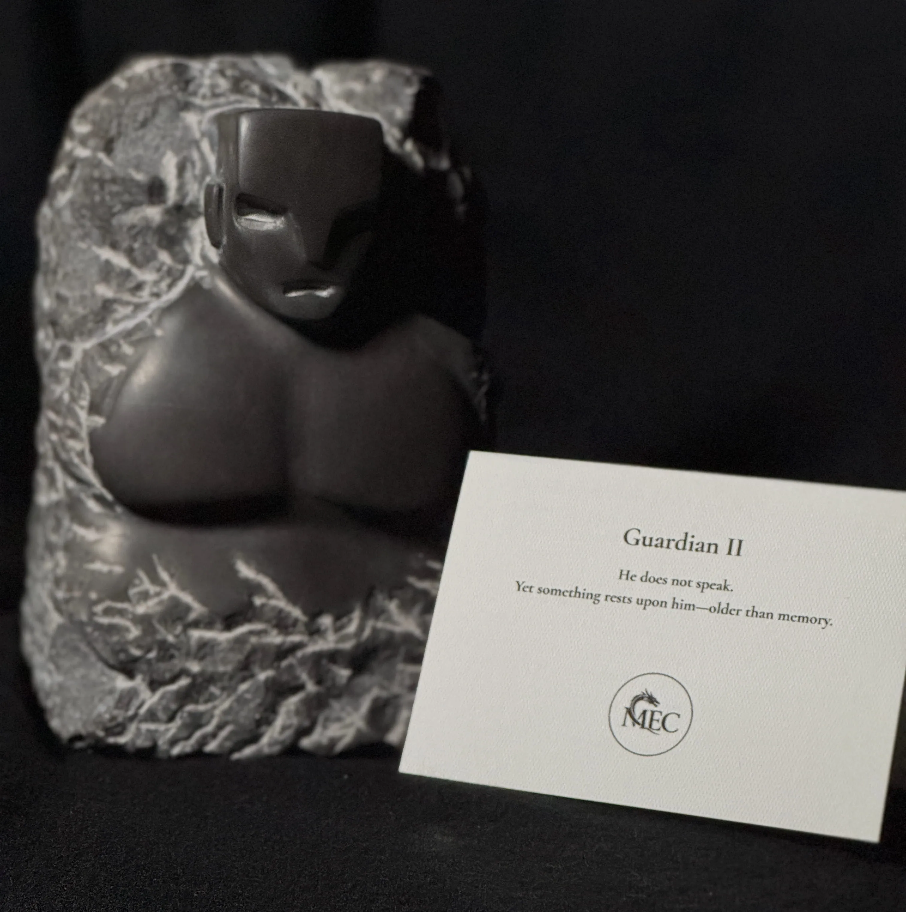 Abstract dark stone sculpture of a face and torso with a card saying 'Guardian II' and a short poem.