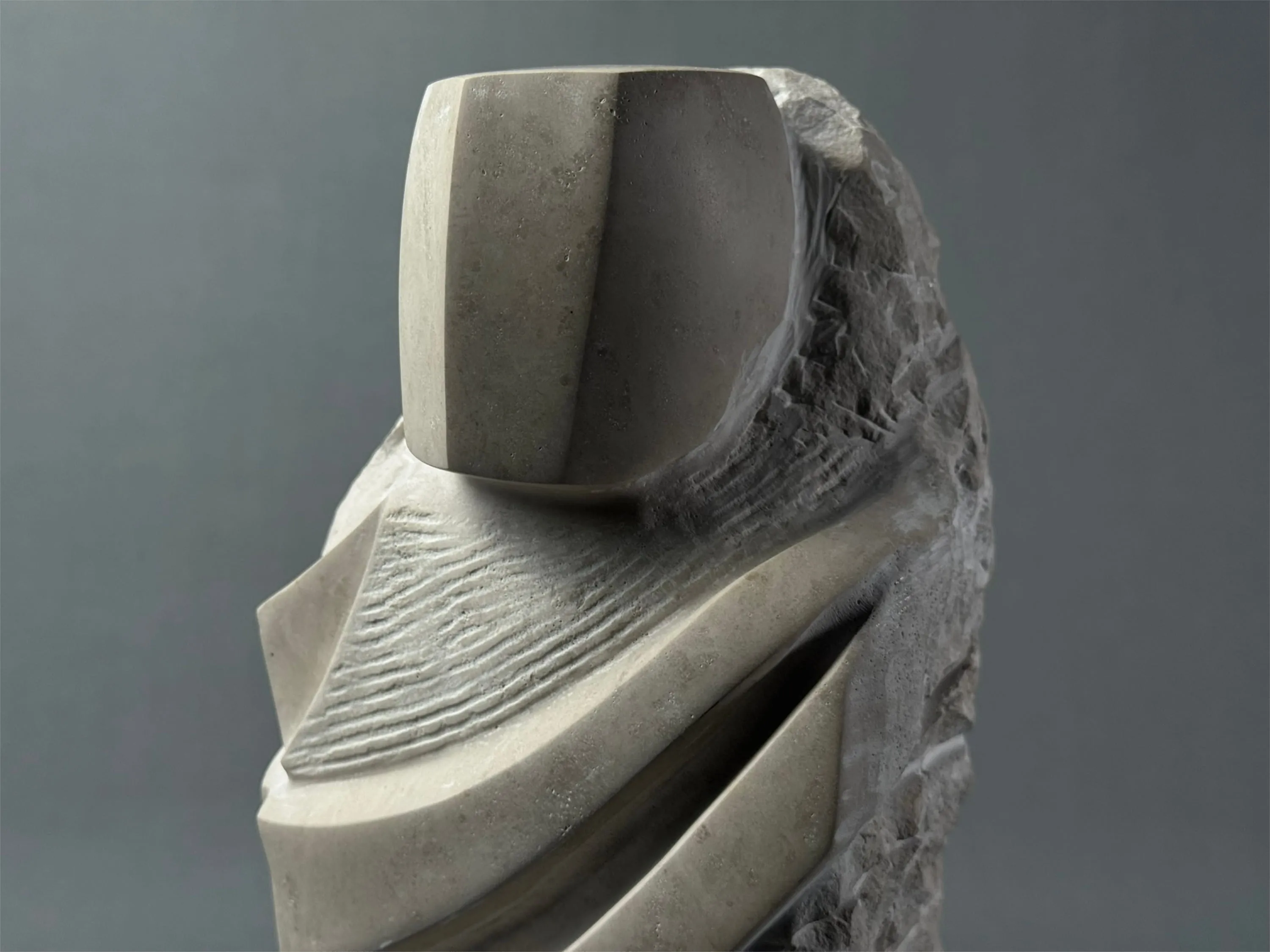 Abstrakte Skulptur aus Stein mit glattem Gesicht und strukturierten, diagonalen Linien.