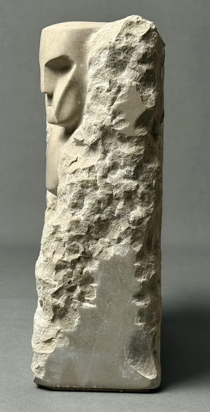 Skulptur aus Stein mit einer Hälfte geglättetem menschlichen Gesicht und der anderen Hälfte grob bearbeitet.