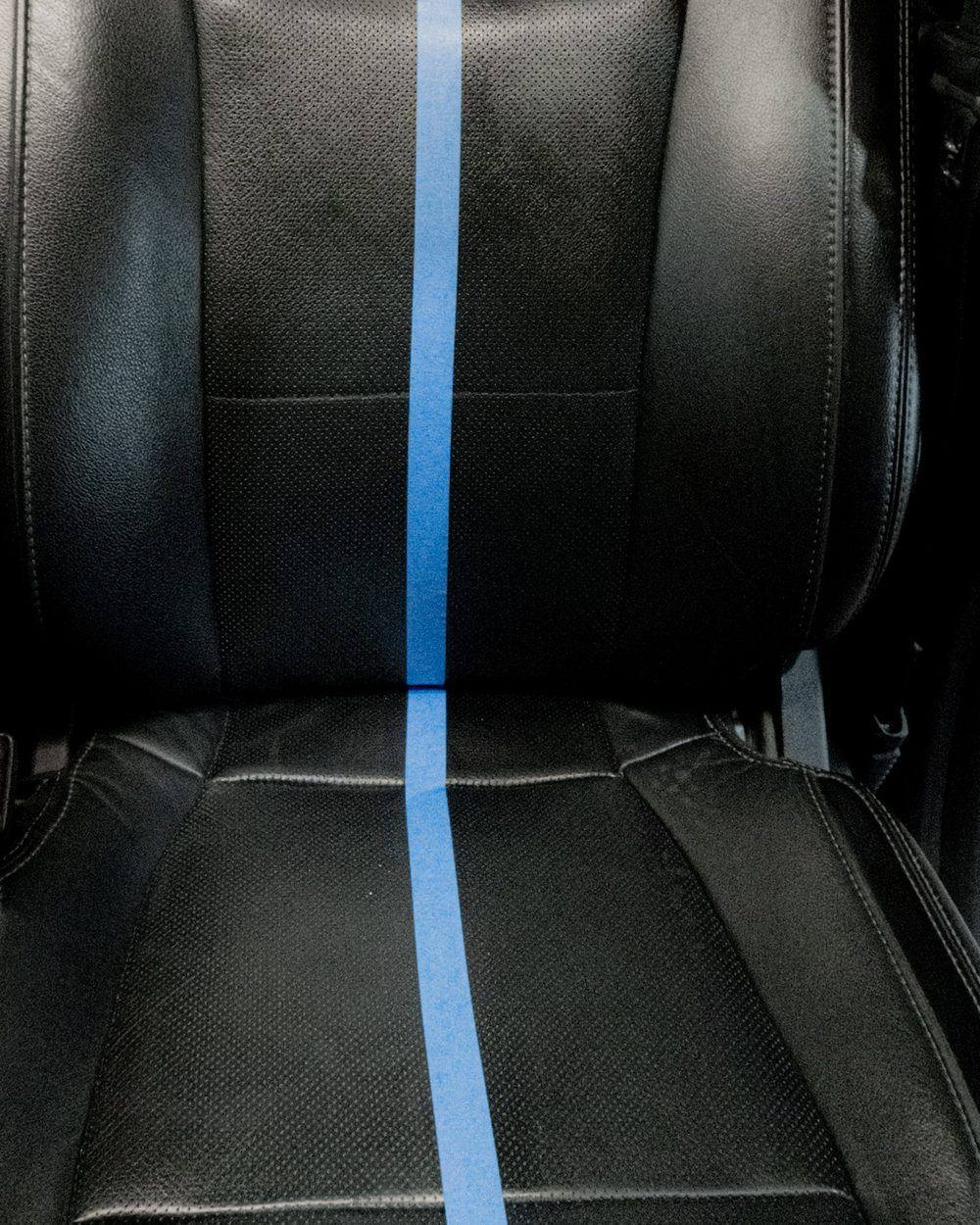 Black perforated leather car seat split with tape line showing untreated half before professional leather conditioning by High Shine Detailing Shakopee MN