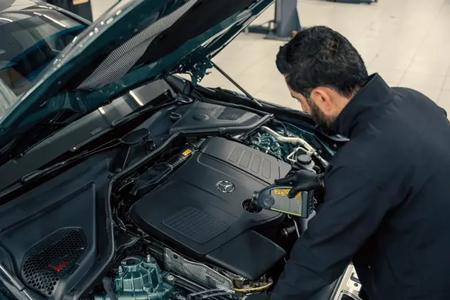 Mann inspiziert den Motorraum eines Autos mit geöffneten Motorhaube in einer Werkstatt.