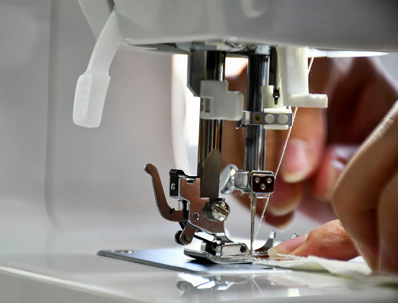 Nähmaschine näht weißen Stoff, Hand führt Stoff unter Nähnadel.