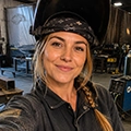 Smiling woman wearing a dark bandana and leather jacket taking a selfie indoors by stage equipment.