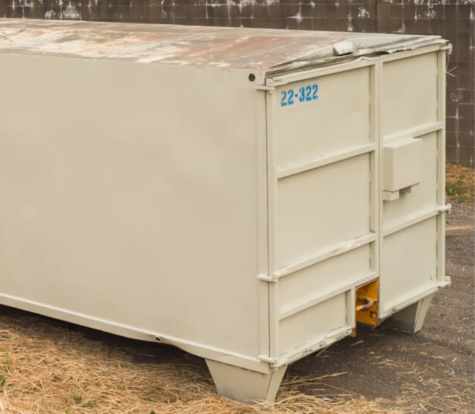 Large beige closed roll-off dumpster container with number 22-322 near a cinder block wall.