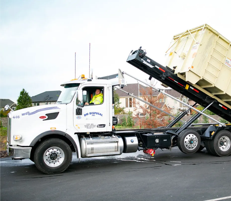White roll-off truck from DM Disposal lifting a large waste container on a suburban street.