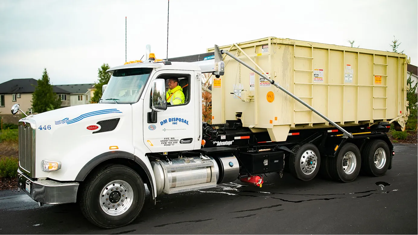 White DM Disposal roll-off truck with beige container parked on a residential street.