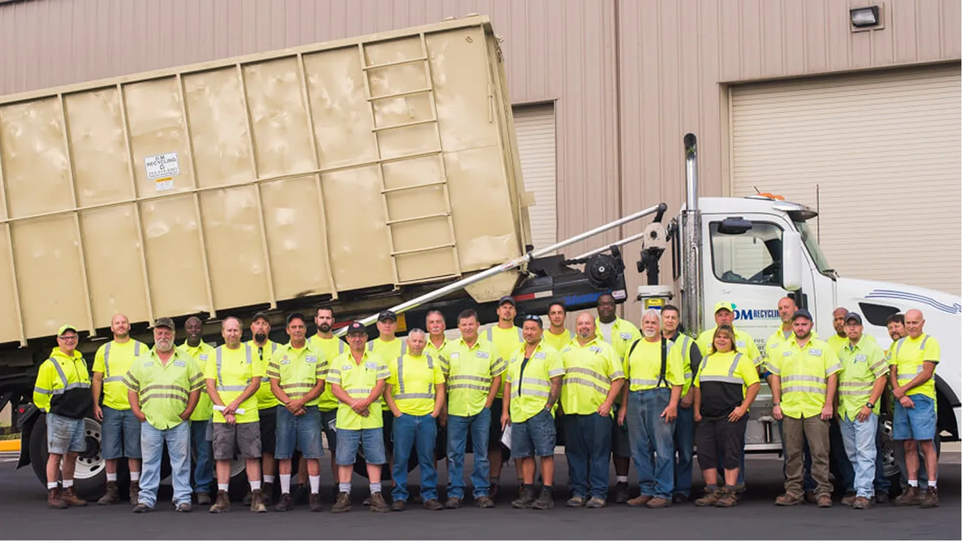 Group of recycling crew in yellow safety vests standing in front of a large roll-off truck.