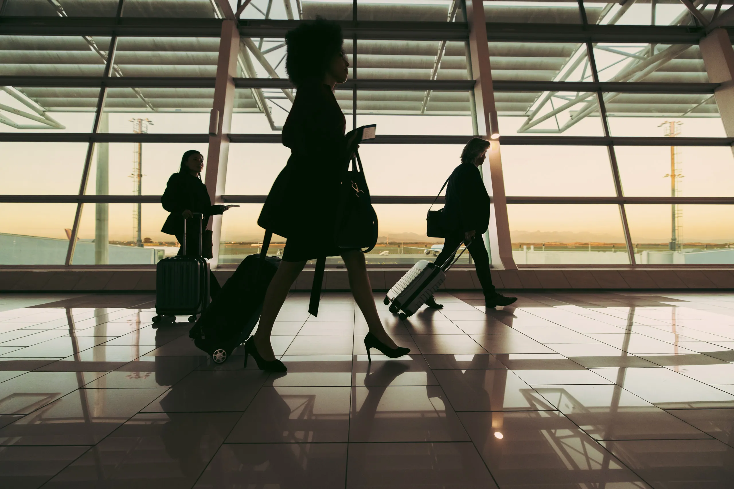 Travelers silhouetted against the windows of an airport terminal