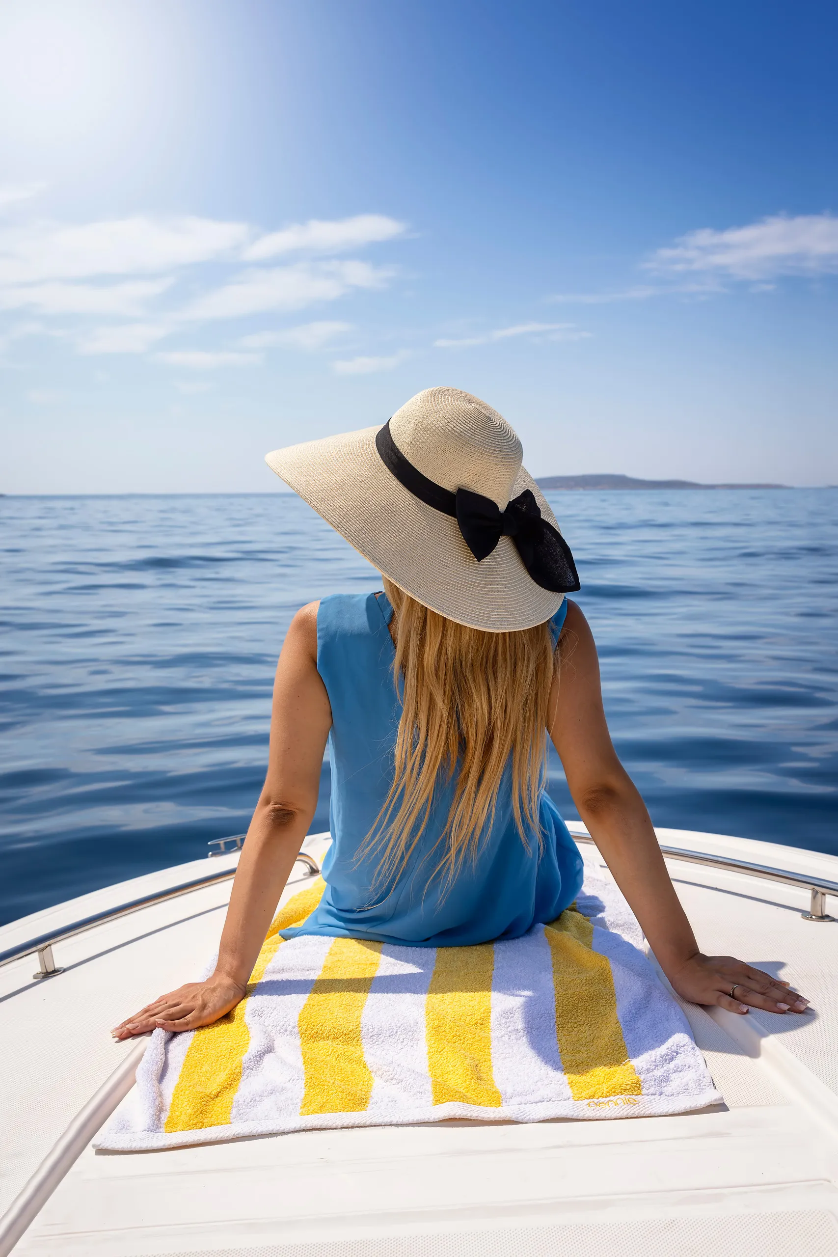 Woman in a sun hat seated at the bow of a boat over calm open sea