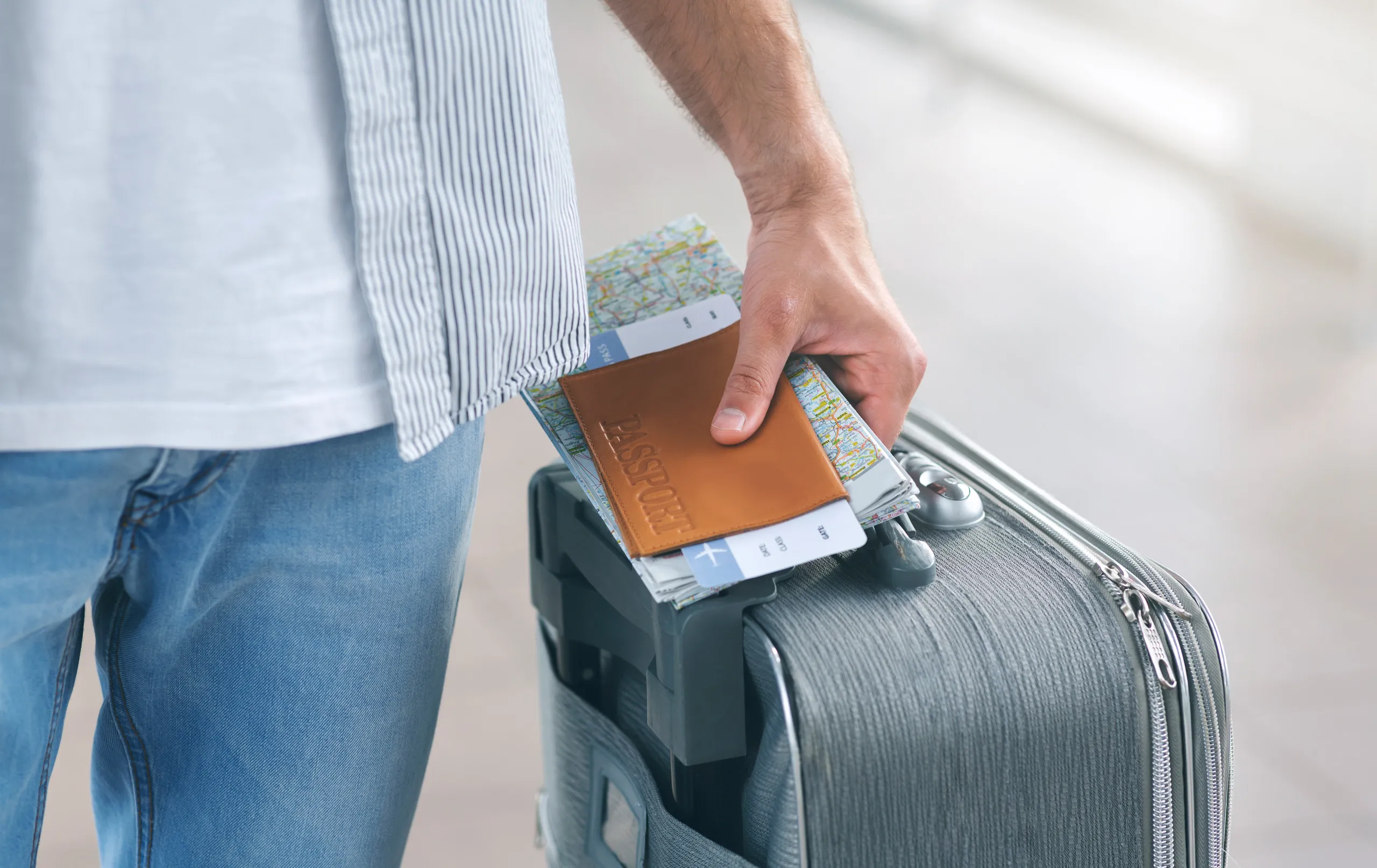 A traveler holding a passport and travel documents beside a suitcase