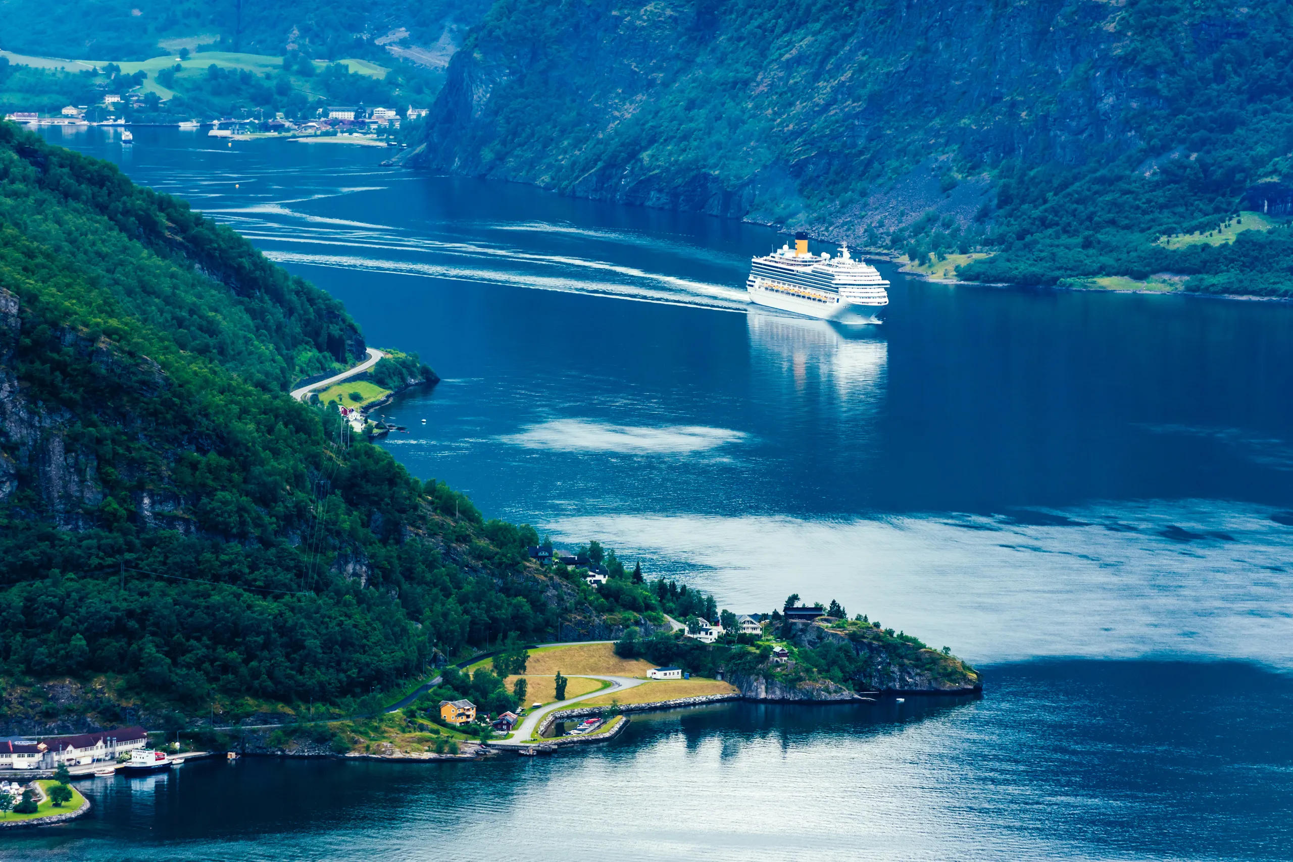 A cruise ship sailing a narrow fjord between steep green cliffs