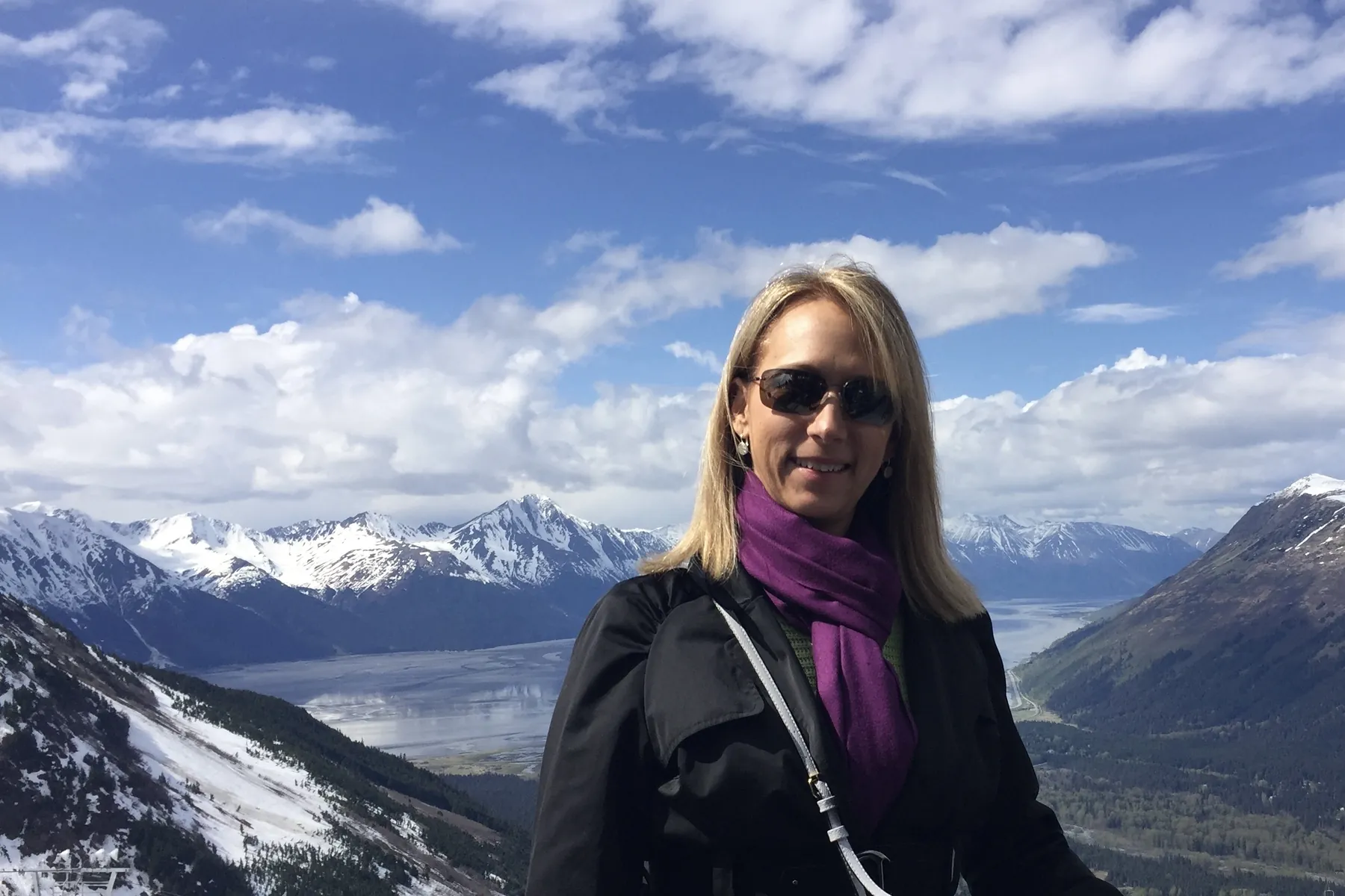 Tina Klump with snow-capped mountains and water behind her in Alaska