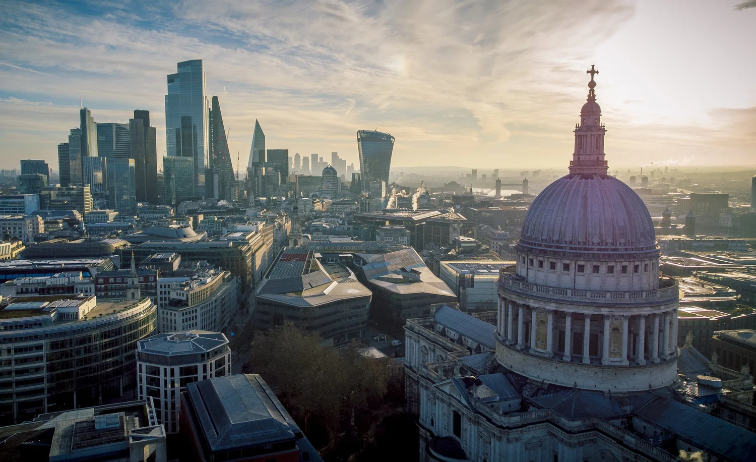 London skyline at sunrise with St. Paul's Cathedral dome in the foreground and modern skyscrapers in the background.