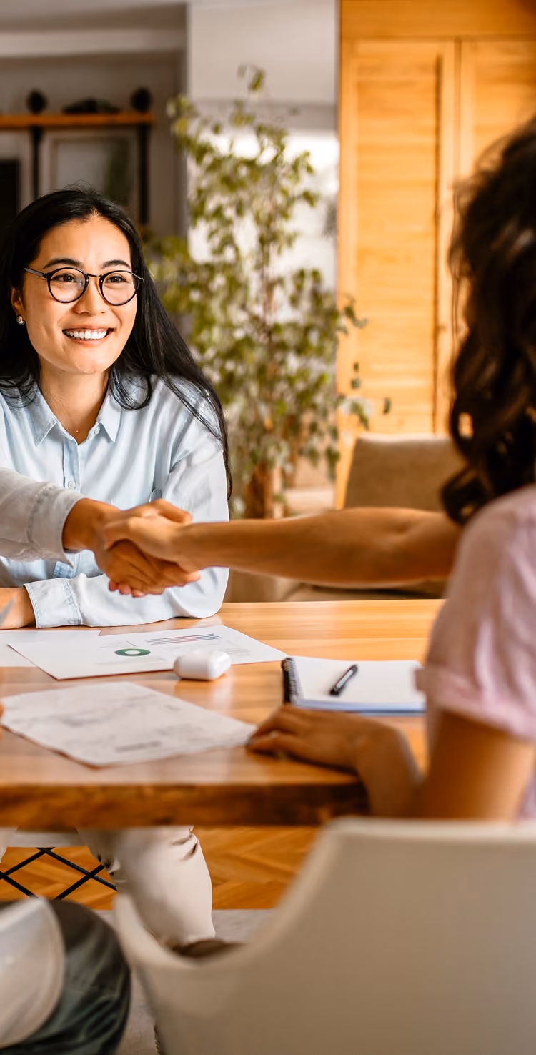 An agent shaking hands with homebuyer couple across table.