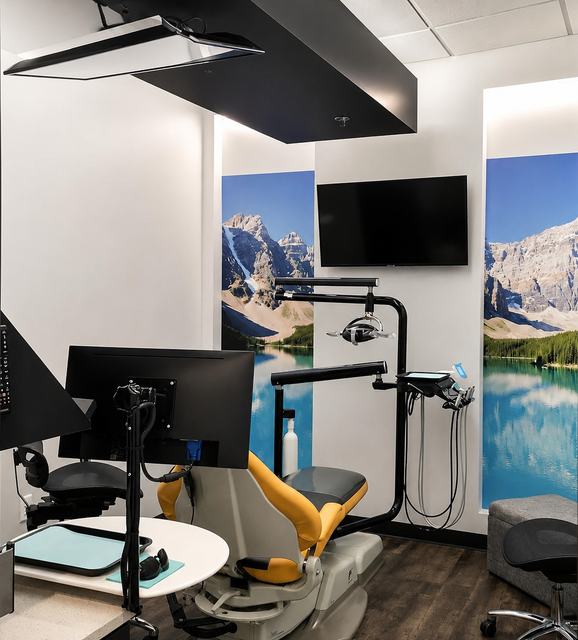 Modern Comfydent Smiles dental treatment room featuring a yellow dental chair, overhead equipment arm, wall-mounted TV, and a floor-to-ceiling mountain lake mural
