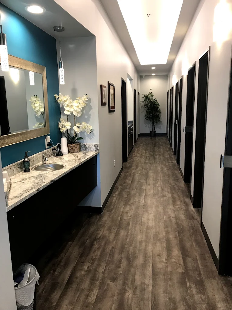 Comfydent Smiles dental office hallway in Bee Cave, TX, with hardwood floors, a marble sink vanity with white orchids, teal accent wall, and a row of treatment room doors.