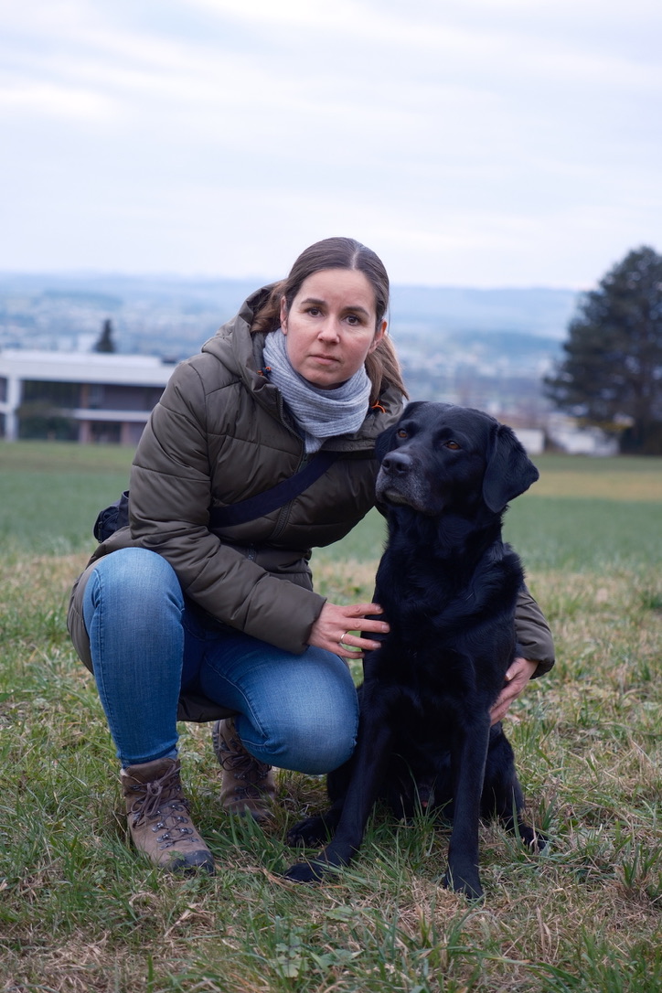 Nina Wolber kniet auf einer Wiese mit ihrem schwarzen Labrador