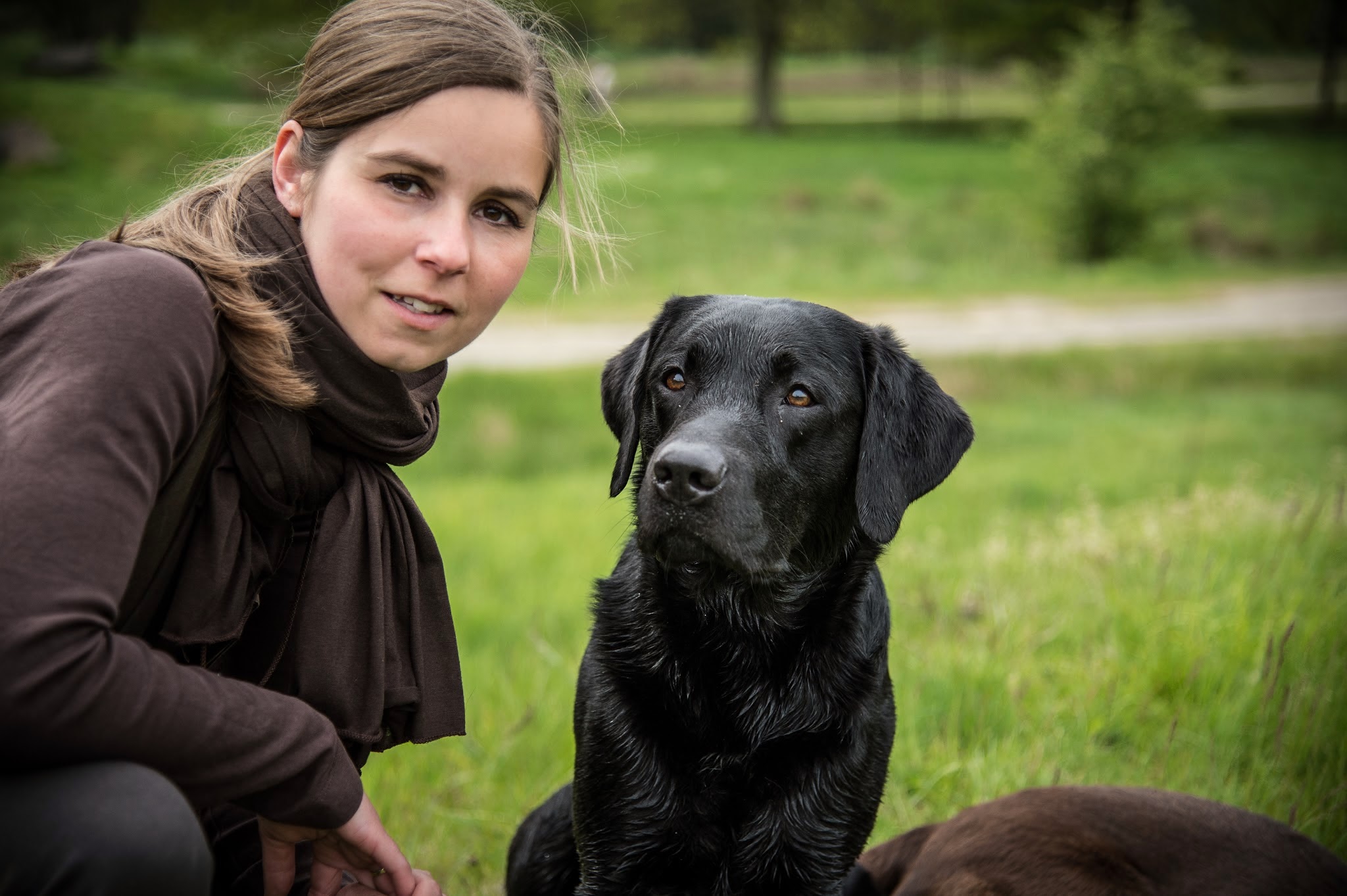 Hundetrainerin Nina Wolber im Portrait neben schwarzem Labrador auf der Wiese — vertrauensvolle Beziehung als Grundlage der Verhaltensberatung