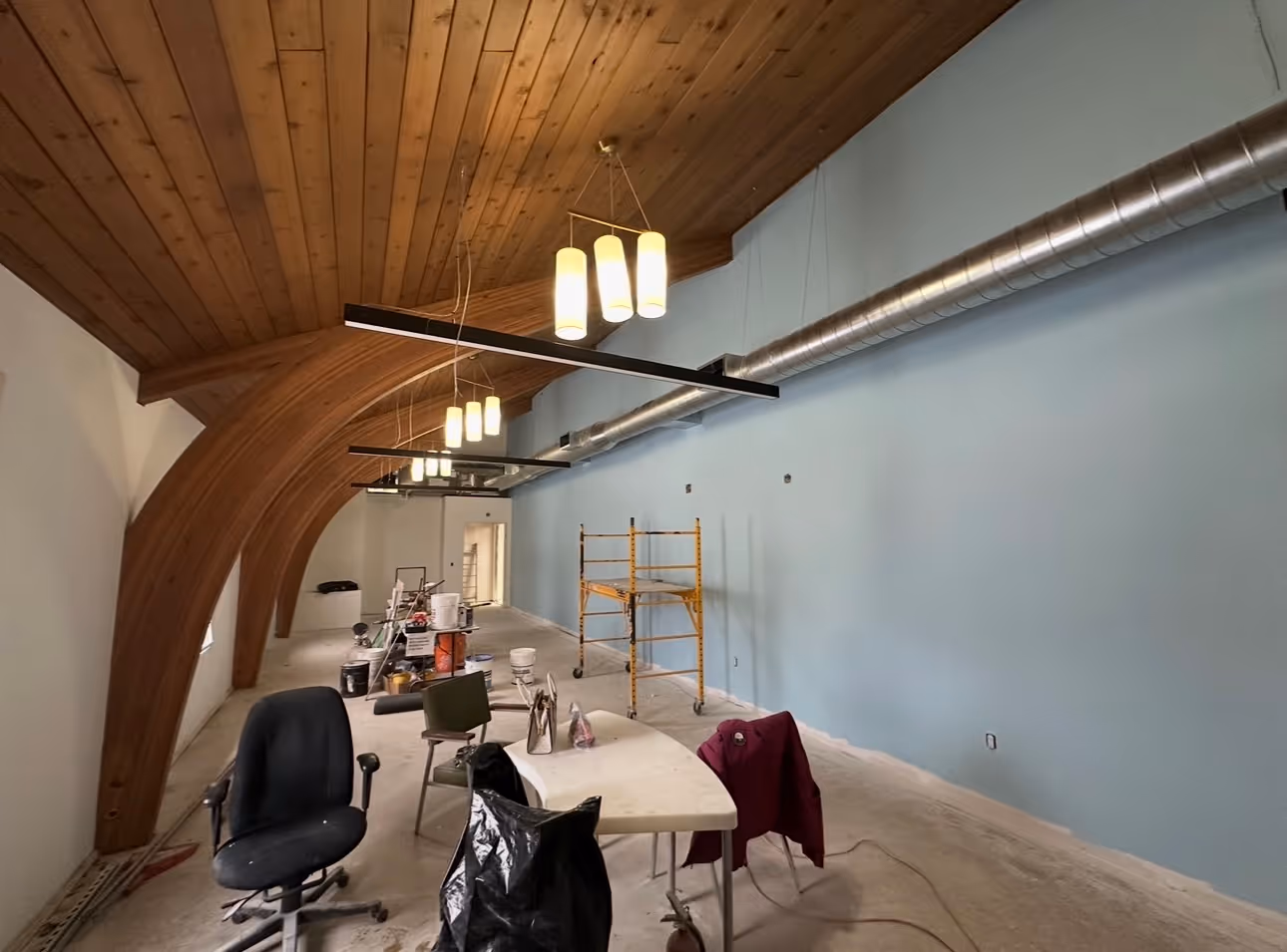 Room under renovation with curved wooden ceiling, blue wall, scaffolding, and furniture scattered.