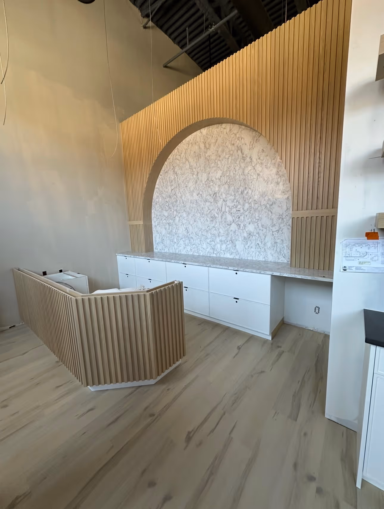 Modern interior with light wood flooring, a white cabinet with marble countertop, and a wood-paneled arch feature wall.