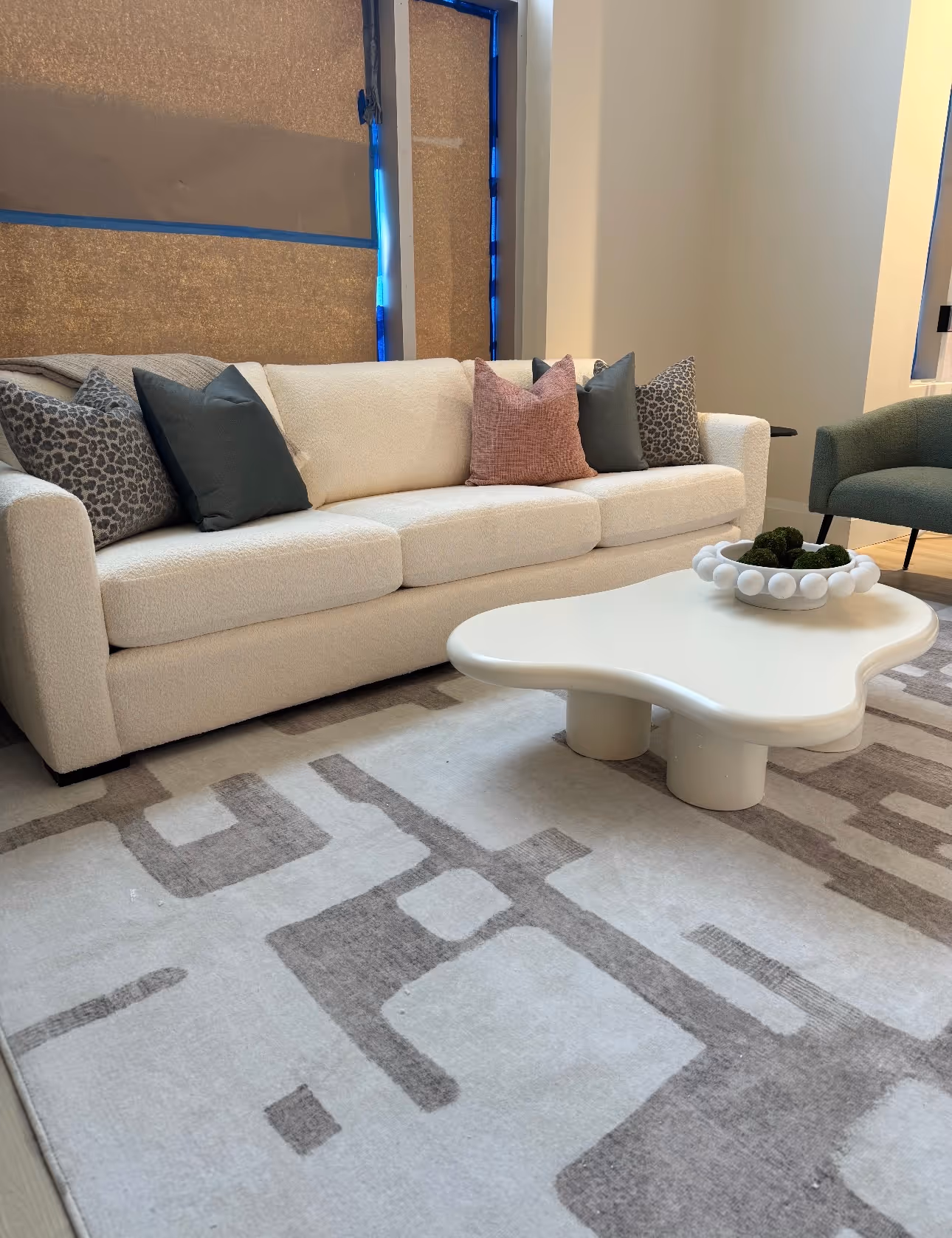 Modern living room with cream sofa, assorted throw pillows, white abstract coffee table, and patterned rug.