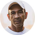 Portrait of a middle-aged man wearing a white cap and dark shirt against a light background.