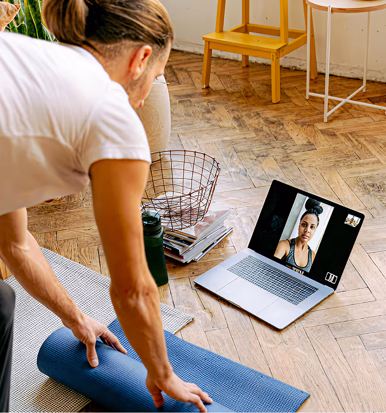 Person rolling up a yoga mat during a video call workout session on a laptop.