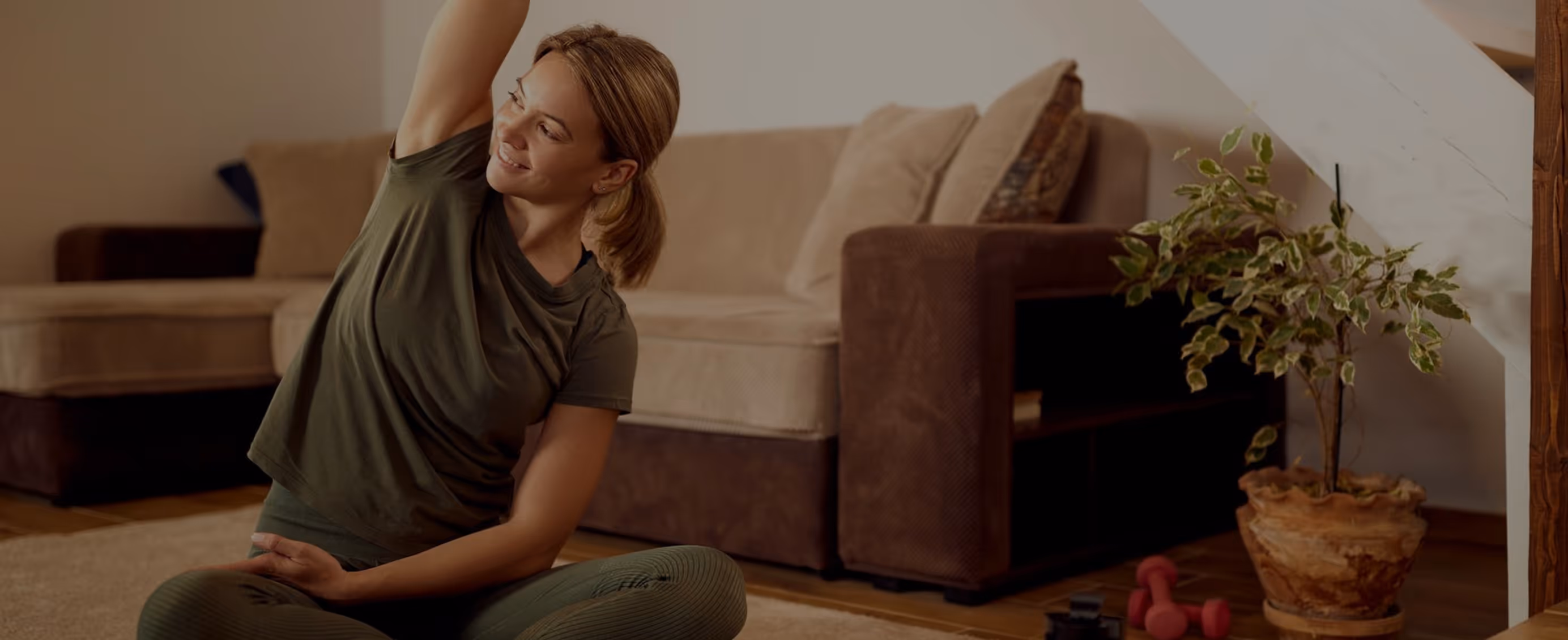 Woman sitting cross-legged on a rug stretching her arm up in a cozy living room.
