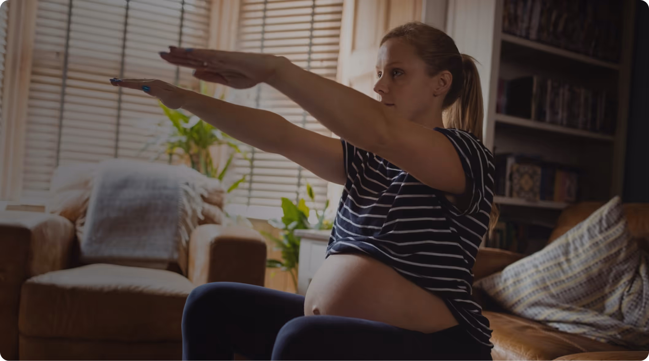 Pregnant woman in striped shirt exercising indoors with arms extended forward.
