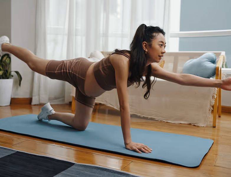 Pregnant woman in activewear doing bird dog yoga pose on blue mat in bright living room.
