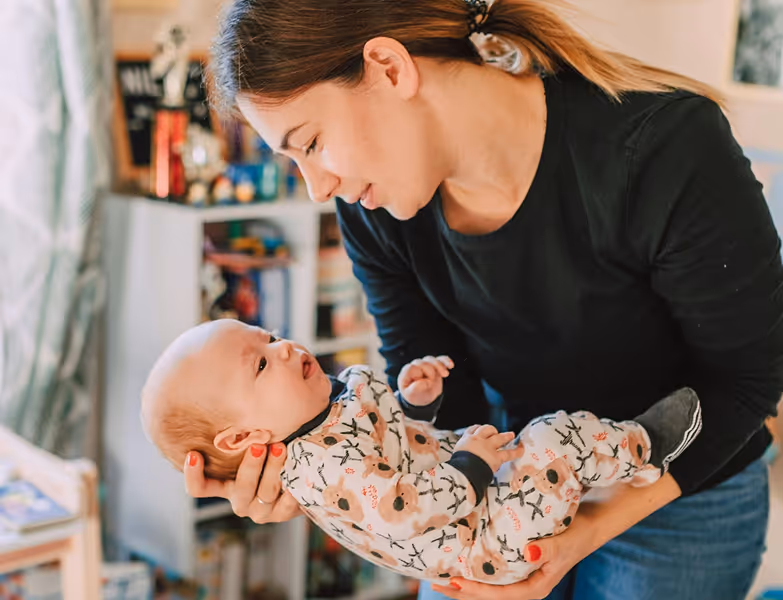 Woman holding baby wearing floral pajamas, looking at each other in a cozy room.