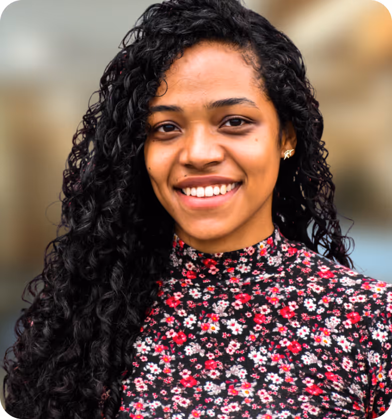 Smiling woman with long curly hair wearing a black floral high-neck top against a blurred background.