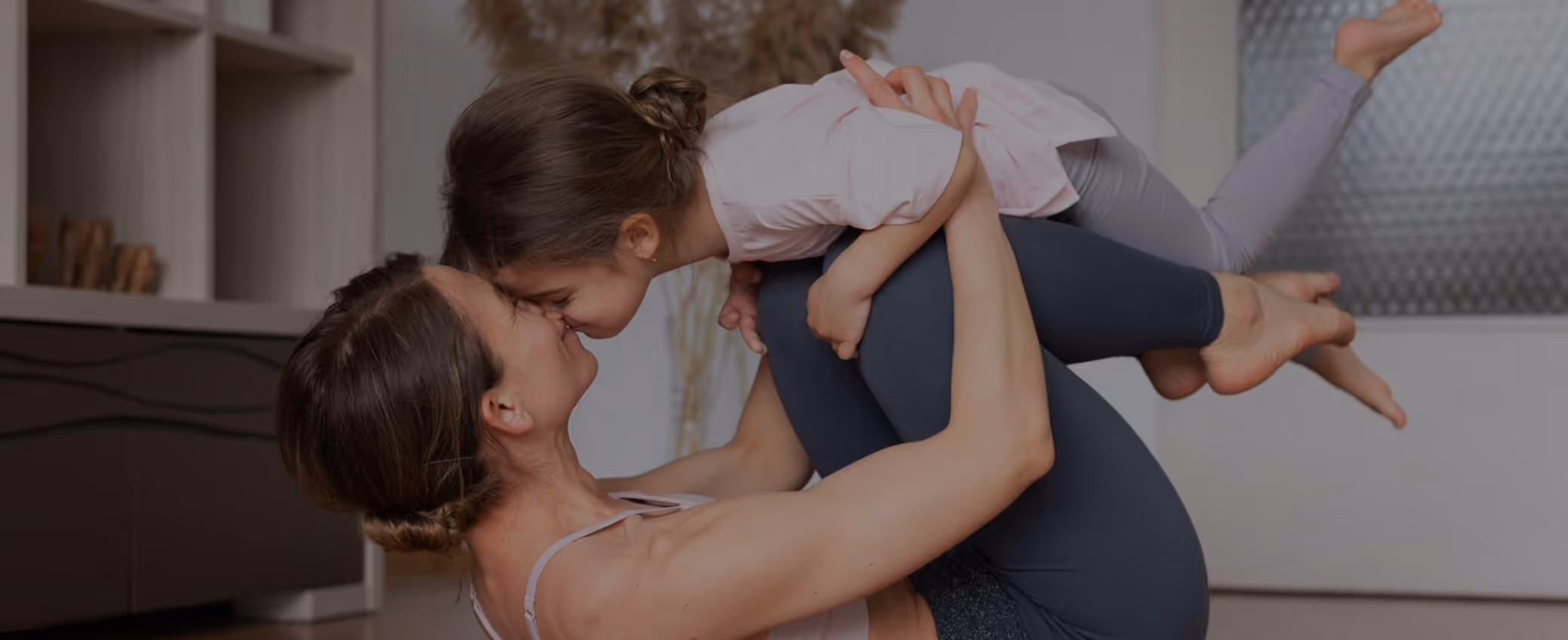 Woman lifting child, touching noses, both smiling, in a cozy indoor setting.