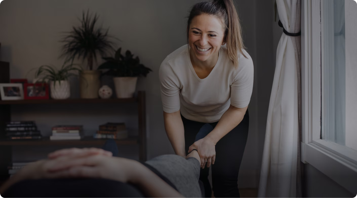 Smiling therapist holding the ankle of a person lying down during a therapy session.