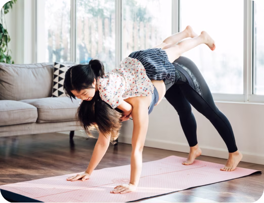 Woman doing yoga plank pose carrying a smiling child on her back inside a bright living room.