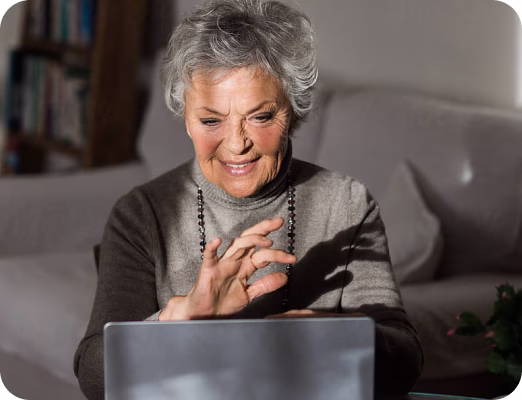 Smiling elderly woman using a laptop in a cozy room with soft lighting.