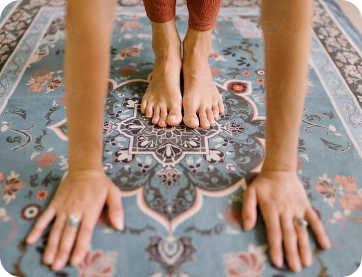 Person's bare feet and hands placed on a patterned blue yoga mat during a stretch or pose.
