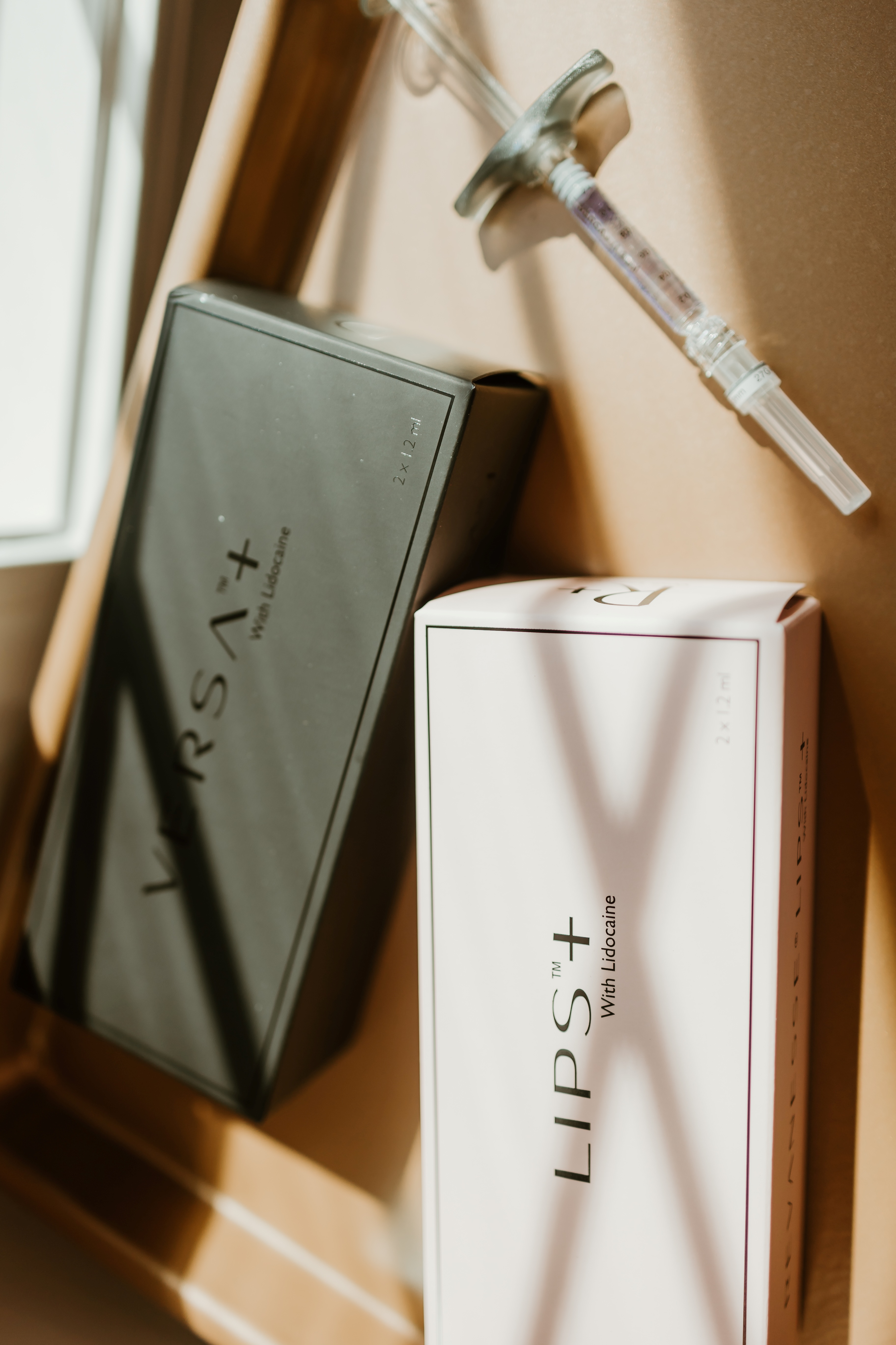 Two boxes labeled 'LIPS+' with Lidocaine text next to a filled syringe on a table in natural light.